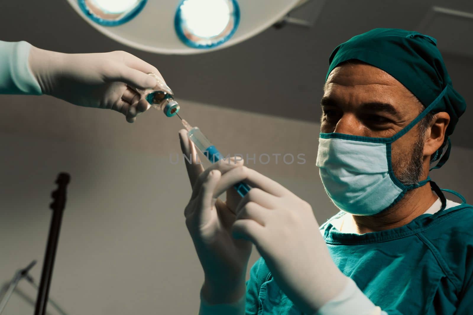 Surgeon fill syringe from medical vial for surgical procedure at sterile operation room with assistance nurse. Doctor and medical staff in full protective wear for surgery prepare anesthesia injection