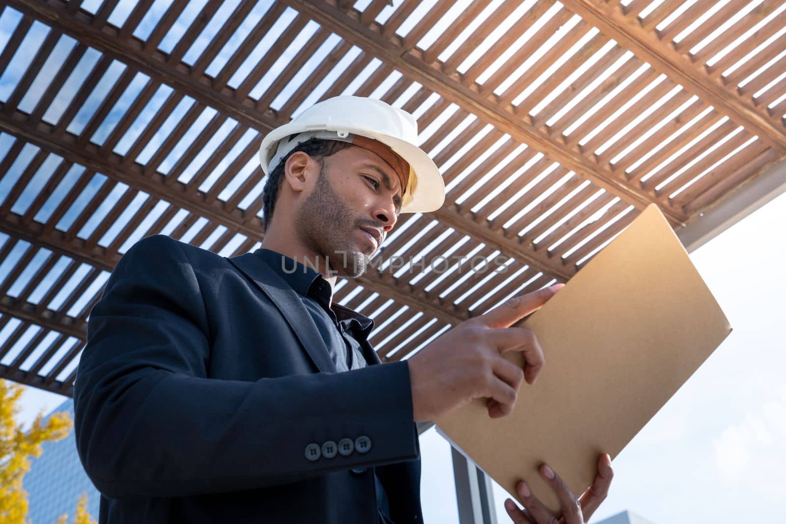 African American businessman manager with construction helmet reviewing blueprints for a project. by PaulCarr
