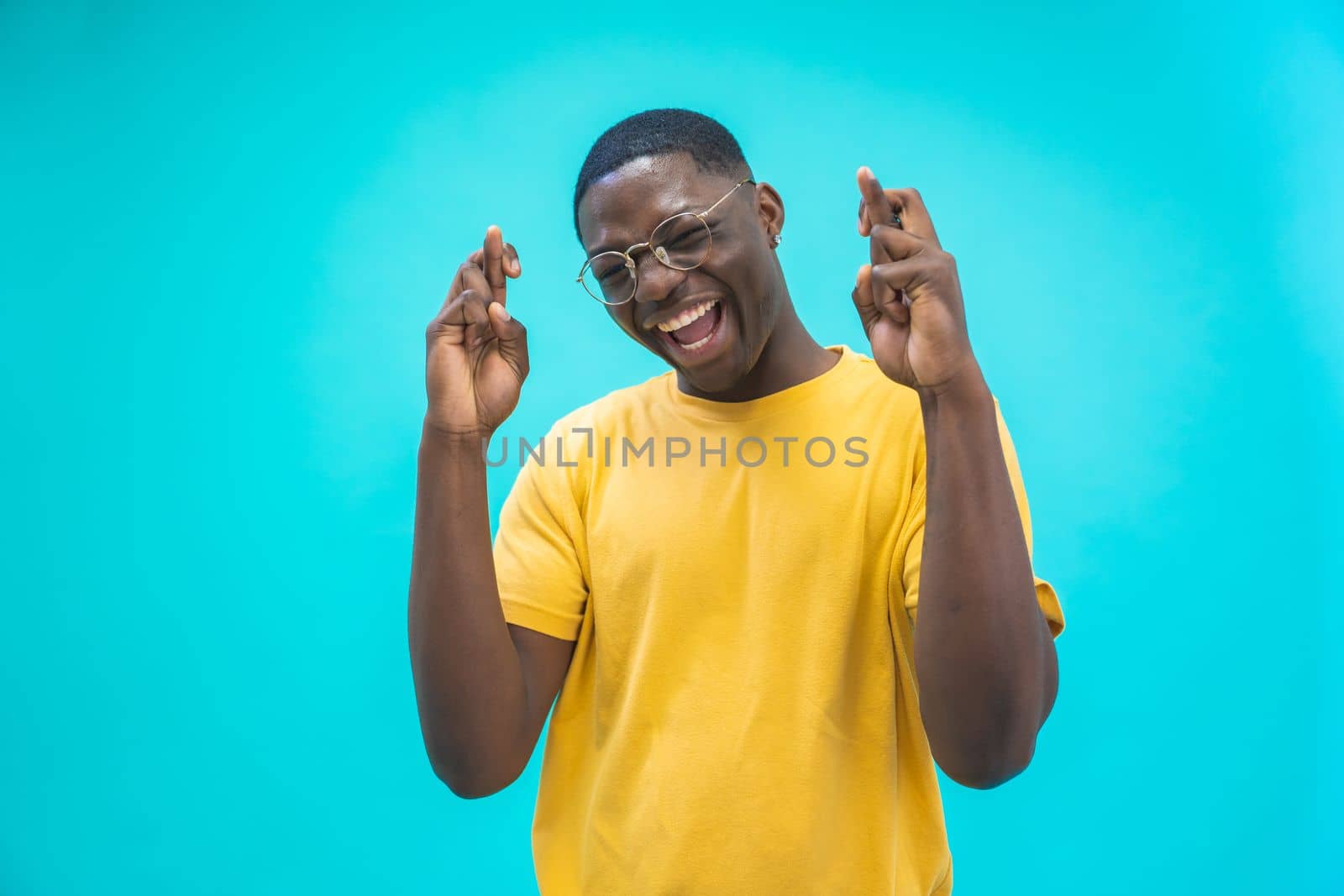 Portrait of a black excited man holding fingers crossed for good luck isolated over blue background. Happy expression High quality photo