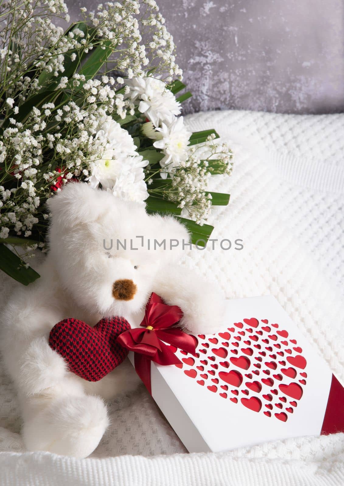 Valentine's day gift, teddy bear with a heart, a box of pralines and a bouquet of flowers on the bed early in the morning. High quality photo