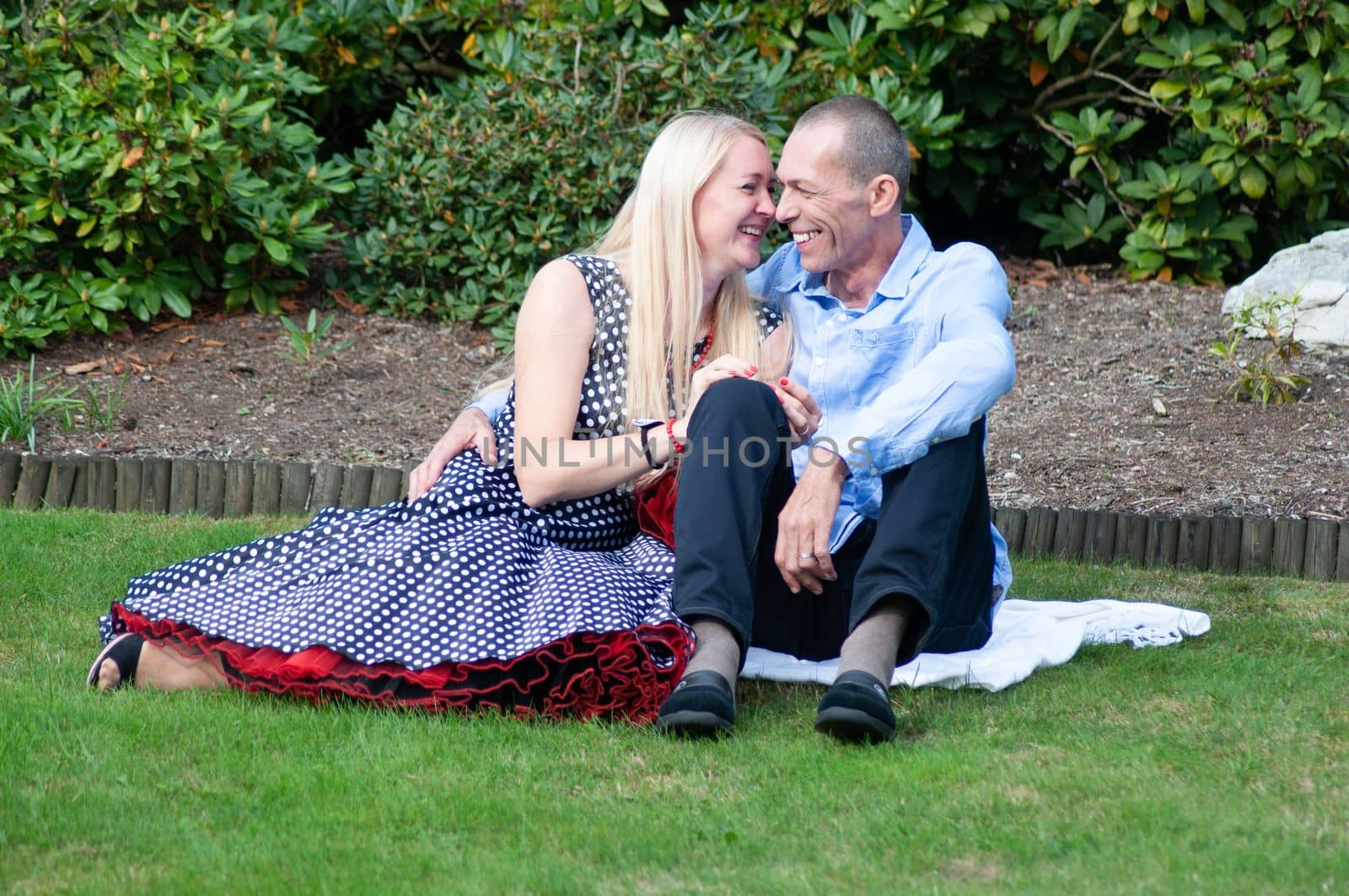a couple of newlyweds a young woman and a man are sitting on the lawn and laughing the woman is dressed in a black dress with white polka dots. High quality photo