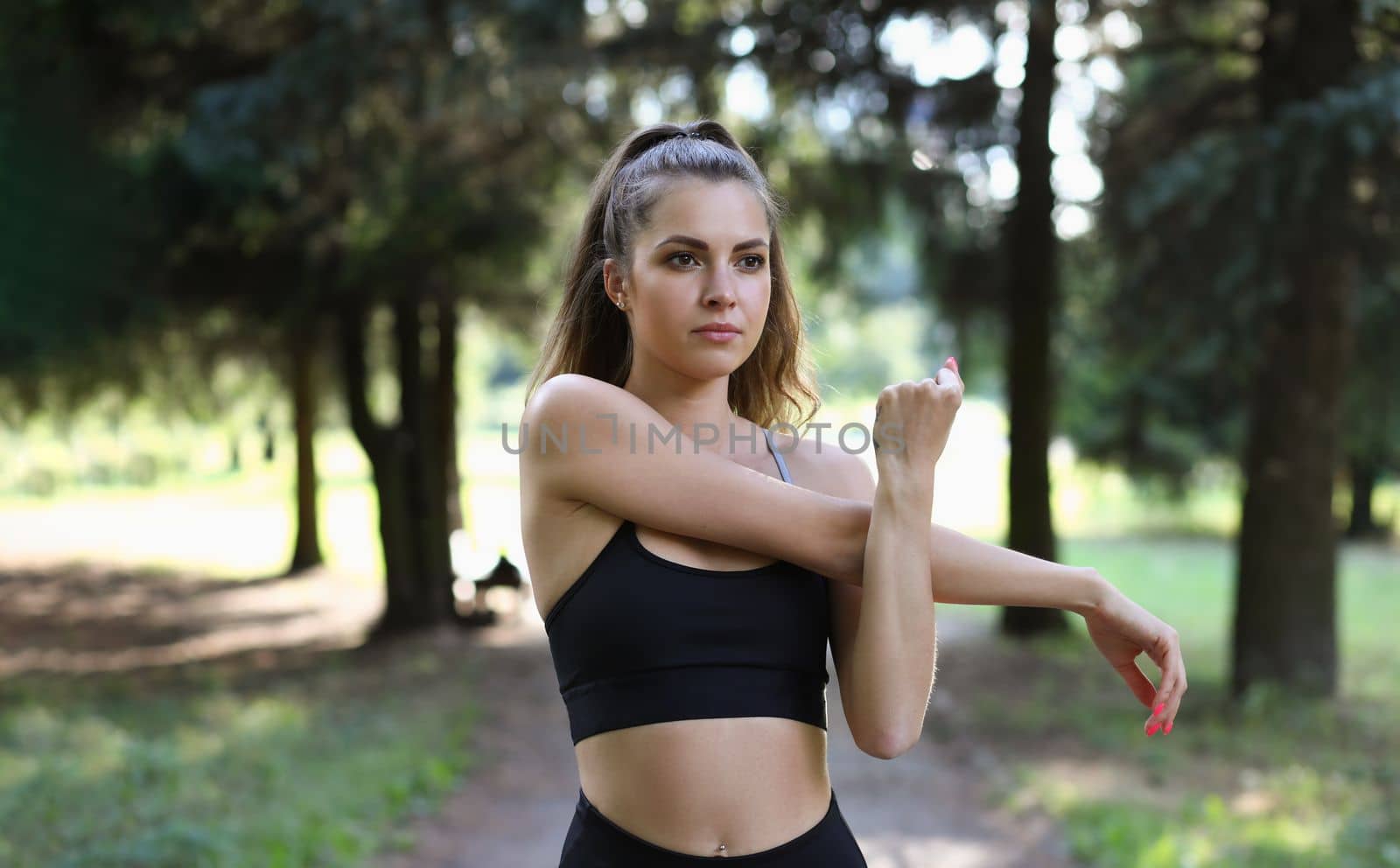 Beautiful woman stretches arms before training in park. Sports and healthy lifestyle to keep fit