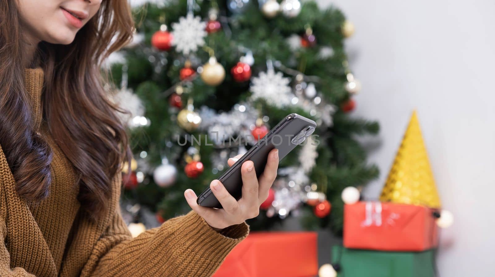 Close up overjoyed asian woman using phone, celebrating success, showing yes gesture, sitting on Christmas tree background at home, received great news, shopping sale, reading message..