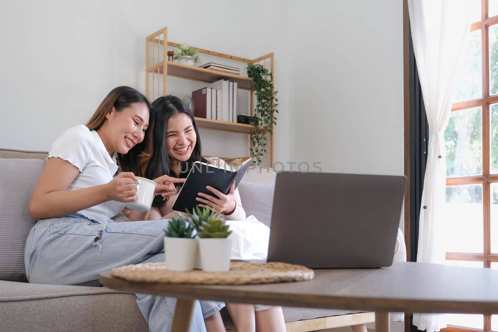 Two female friends reading book while another looking at her smiling playful by wichayada