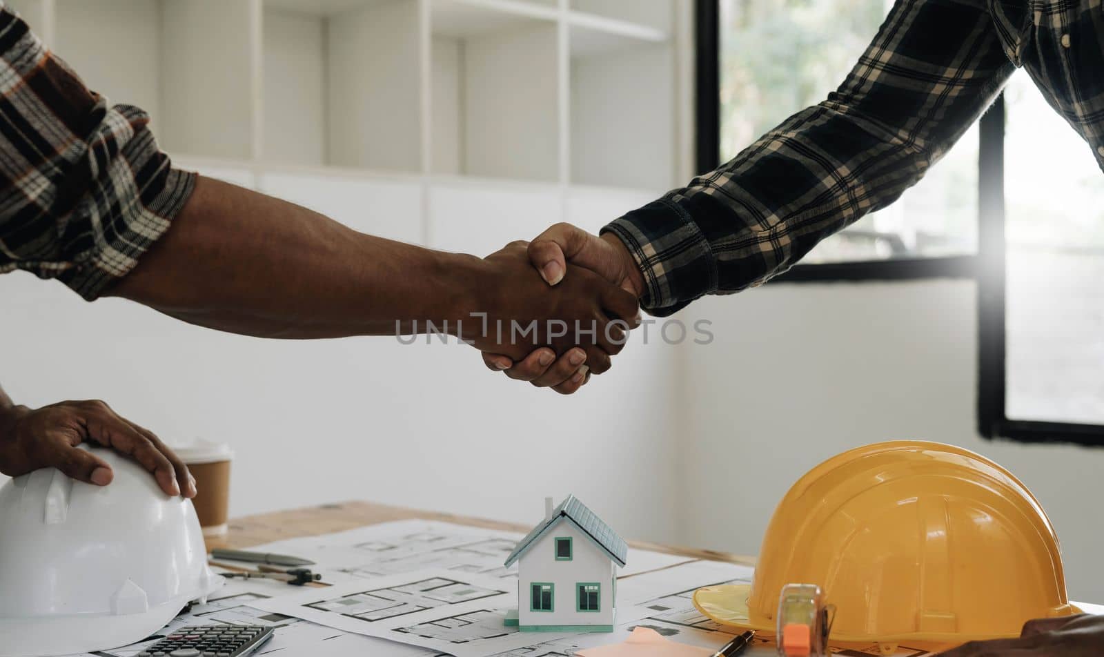 Engineers or architecture shaking hands at construction site for architectural project, holding safety helmet on their hands