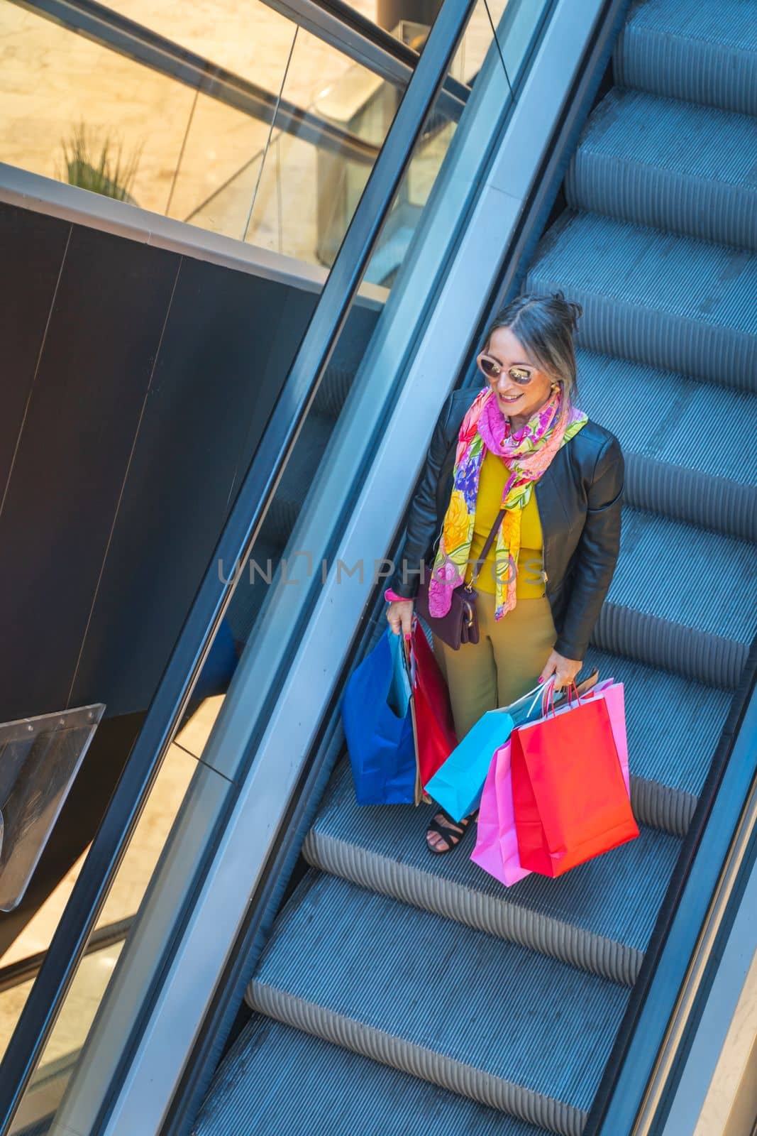 Senior lady with shopping bags on mechanic stairs at mall. Woman riding escalator. High quality 4k footage