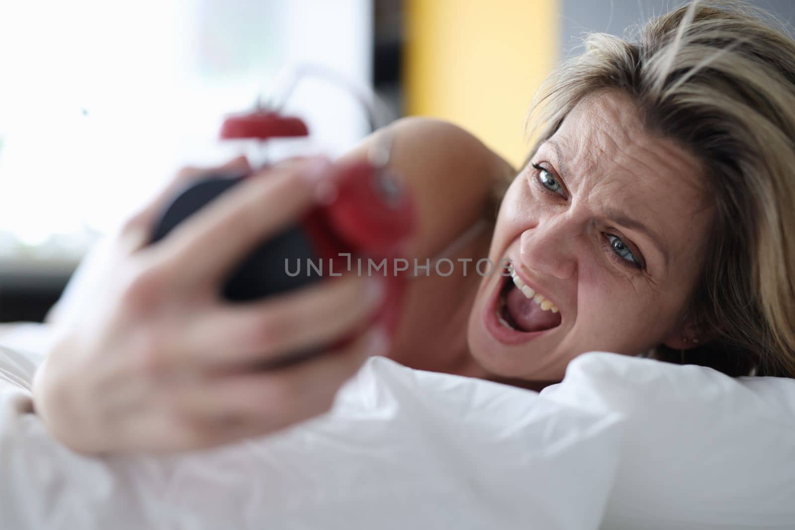 Woman looks at alarm clock and yells to bed. Stress and oversleep for work concept