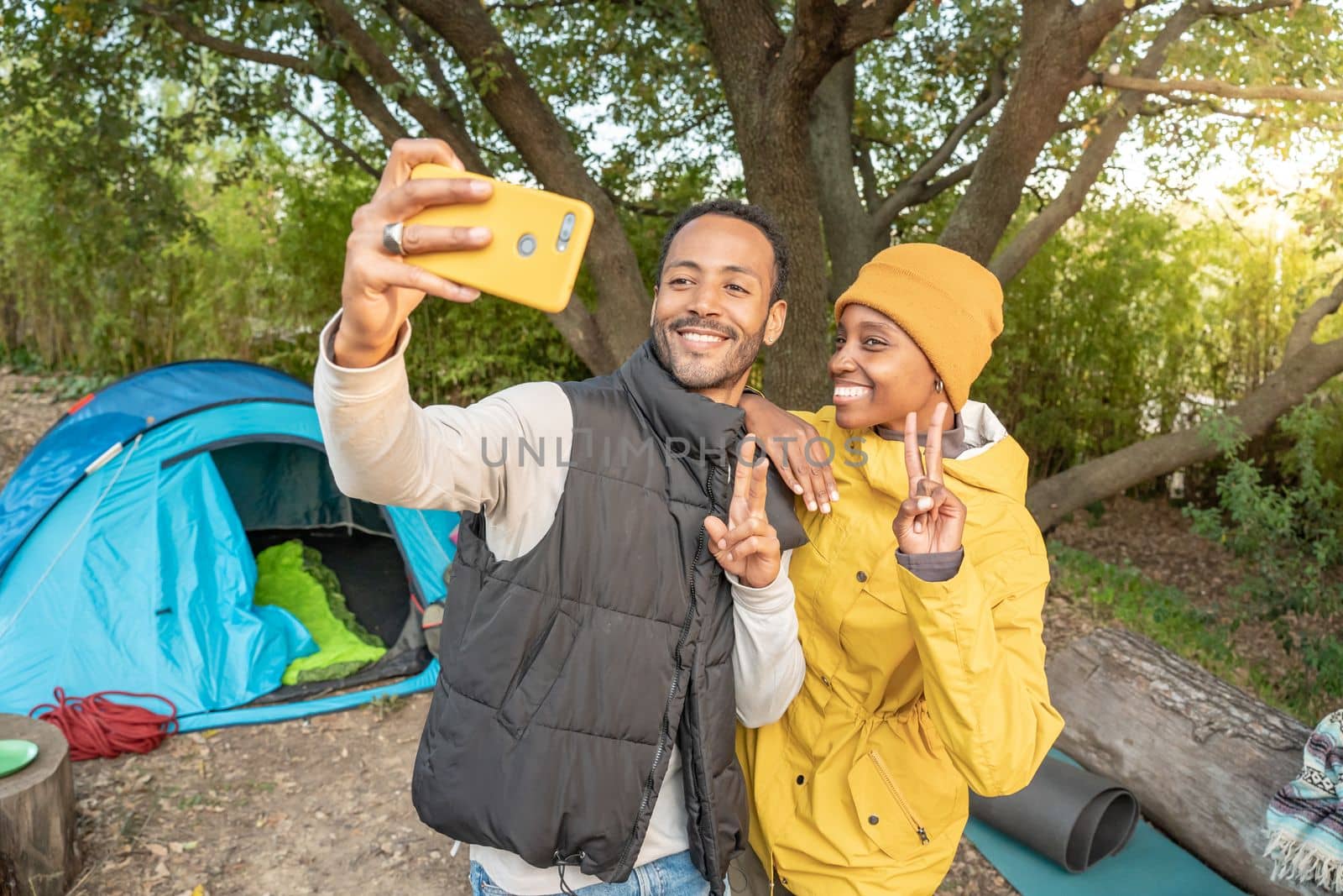 Selfie portrait couple camping - Happy black couple with yellow phone in nature having fun together. During sunny day in autumn or winter. Travel and vacation concept. Wilderness. High quality photo