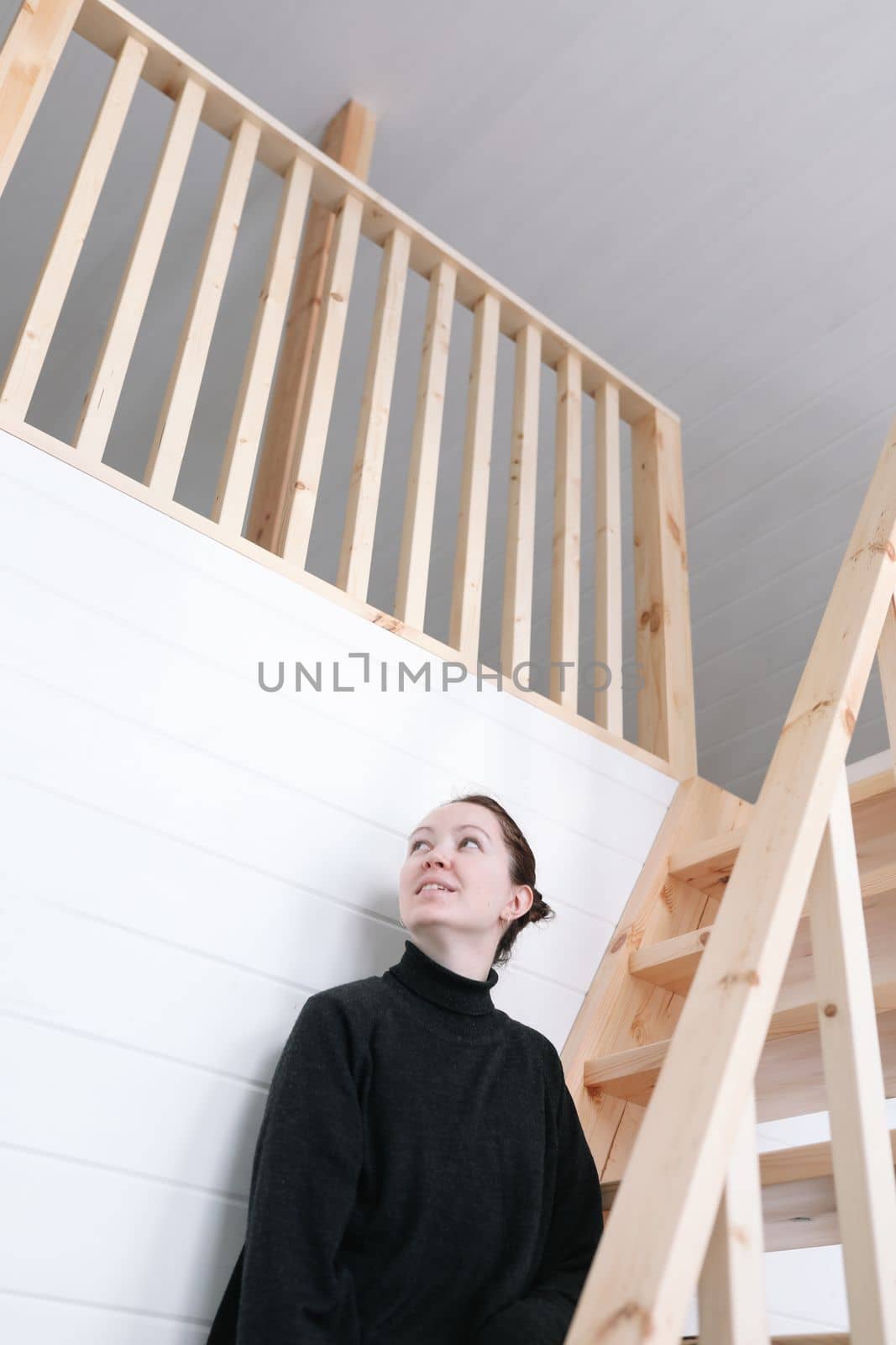 Young woman sitting on wooden stairs in modern house. Attractive brunette at home. 