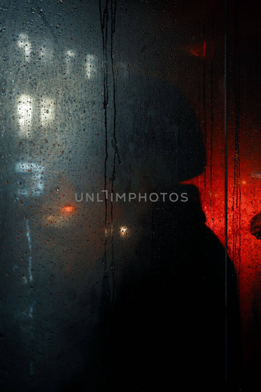 Blackout in Kyiv. Glass showcases with drops of rain and sleet on the streets of Kyiv illuminated by the headlights of cars and with silhouettes of people passing by