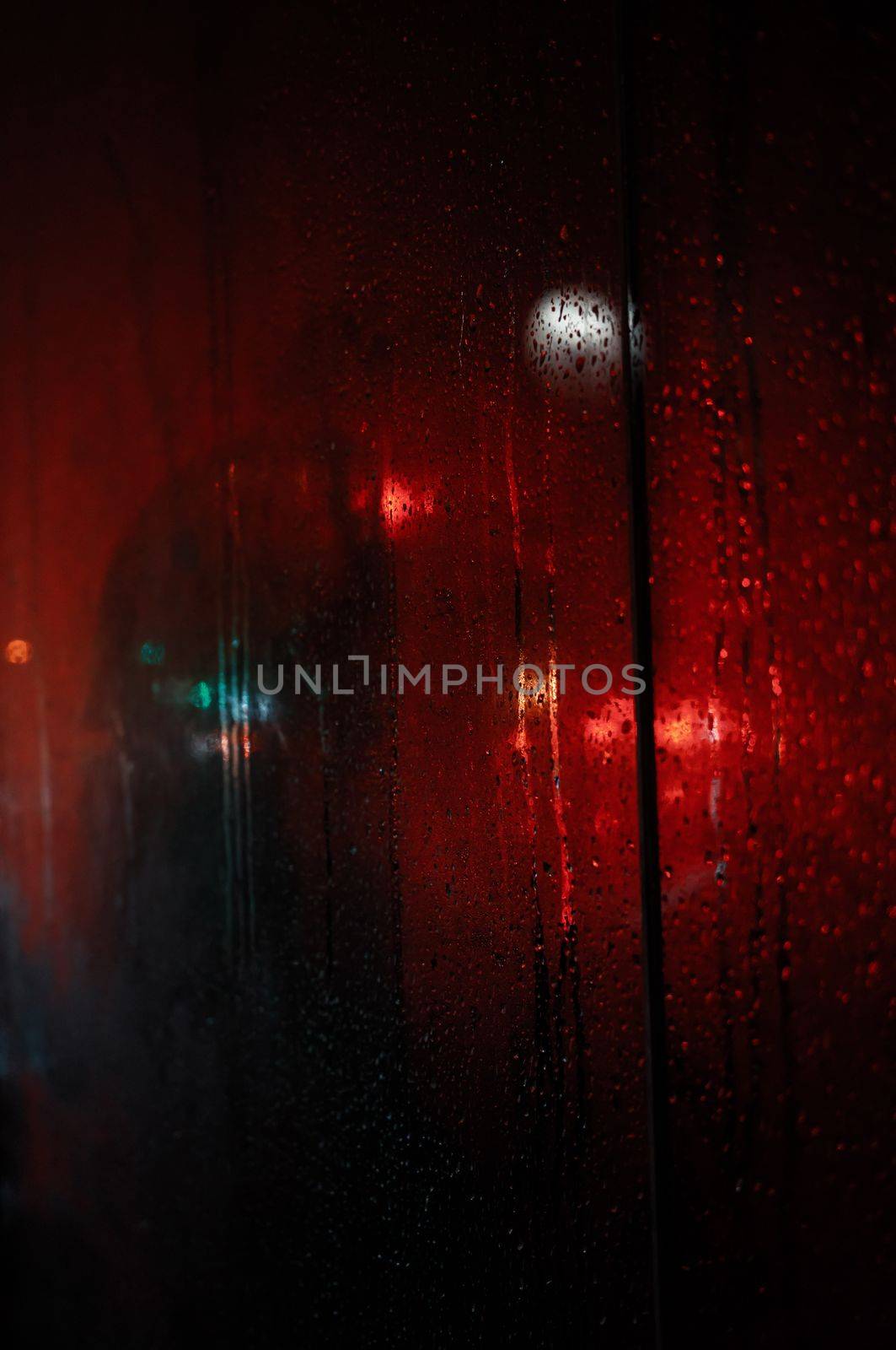 Blackout in Kyiv. Glass showcases with drops of rain and sleet on the streets of Kyiv illuminated by the headlights of cars and with silhouettes of people passing by