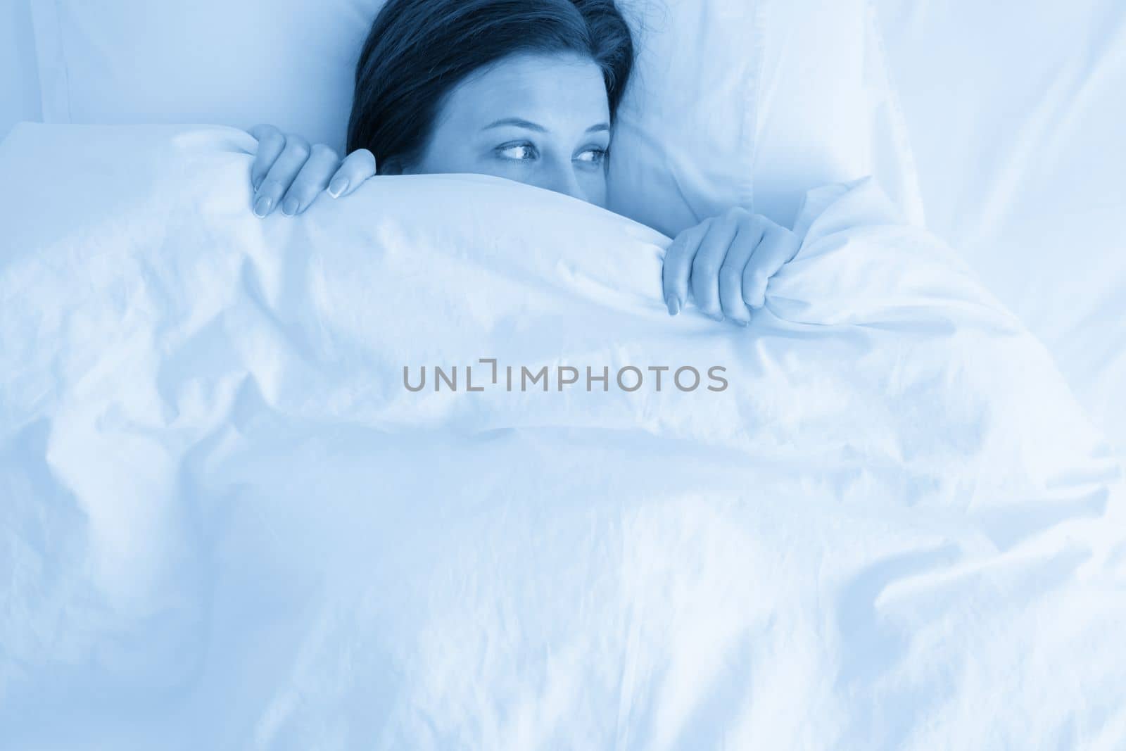 woman in bed looking surprised from under blanket by Mariakray