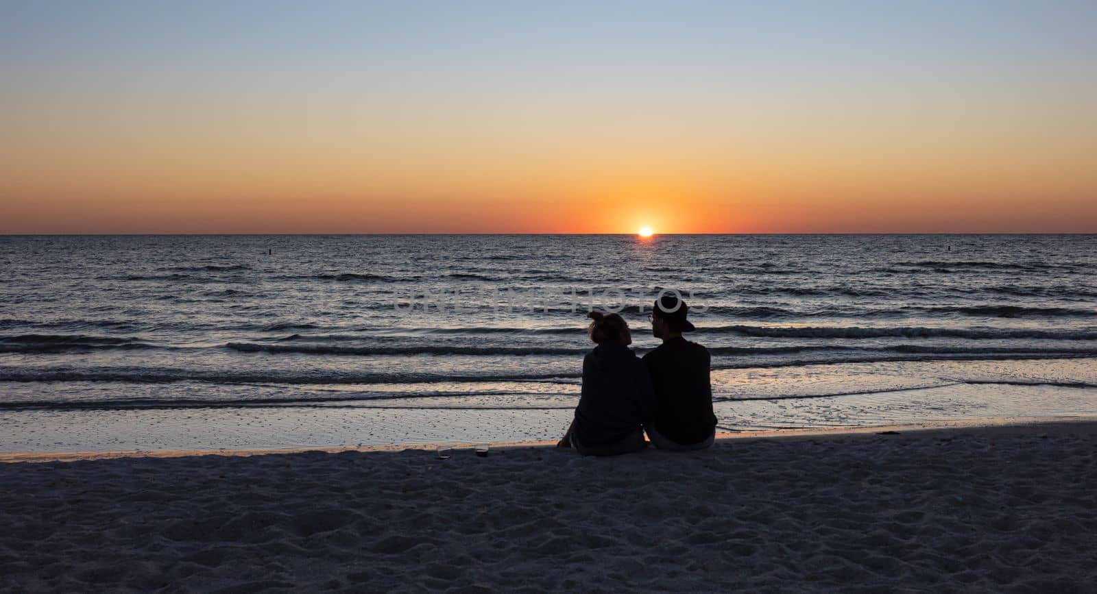 St. Petersburg, Florida, USA - Oct. 22, 2022: Beach lovers watching the sunset sitting on a sandy beach.  Beach scene with couple silhouette. Romantic couple on the beach. St. Petersburg, Florida