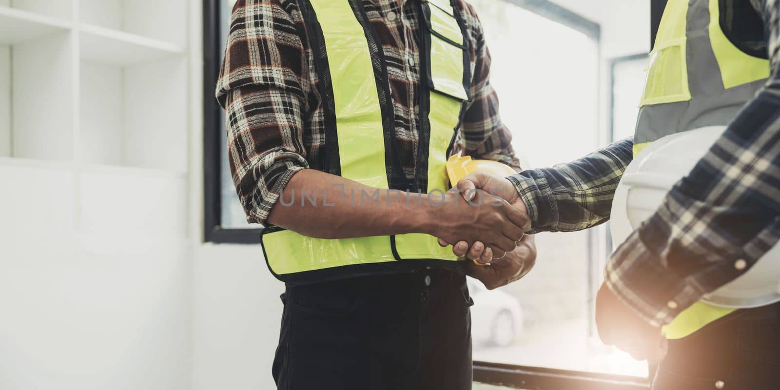 Engineers or architecture shaking hands at construction site for architectural project, holding safety helmet on their hands