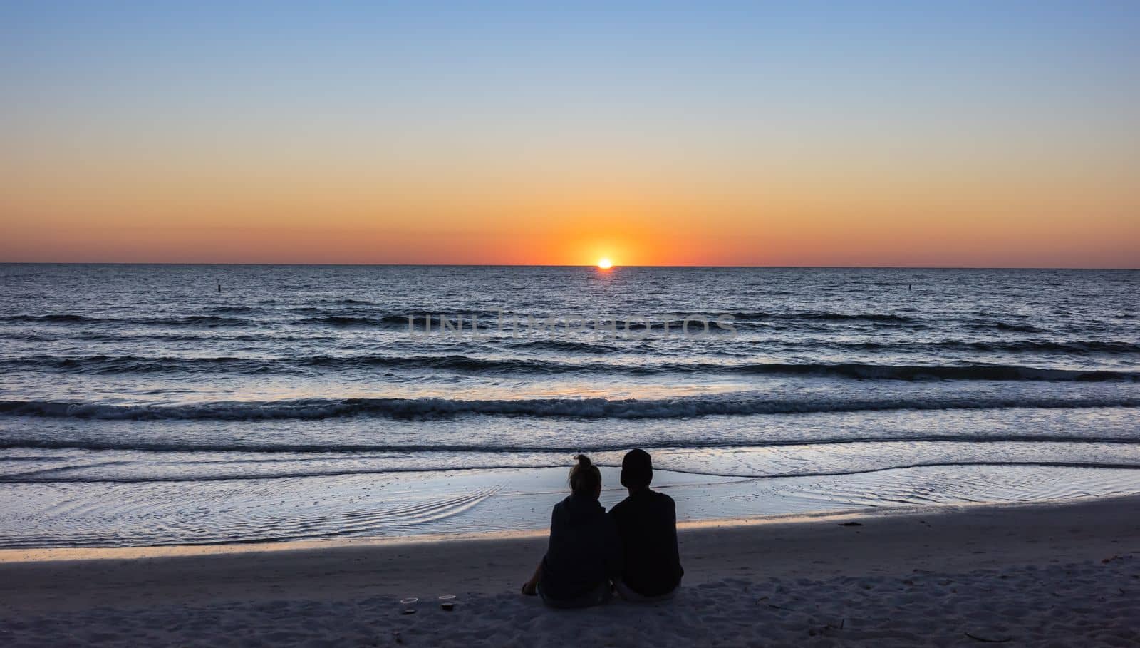 St. Petersburg, Florida, USA - Oct. 22, 2022: Beach lovers watching the sunset sitting on a sandy beach.  Beach scene with couple silhouette. Romantic couple on the beach. St. Petersburg, Florida