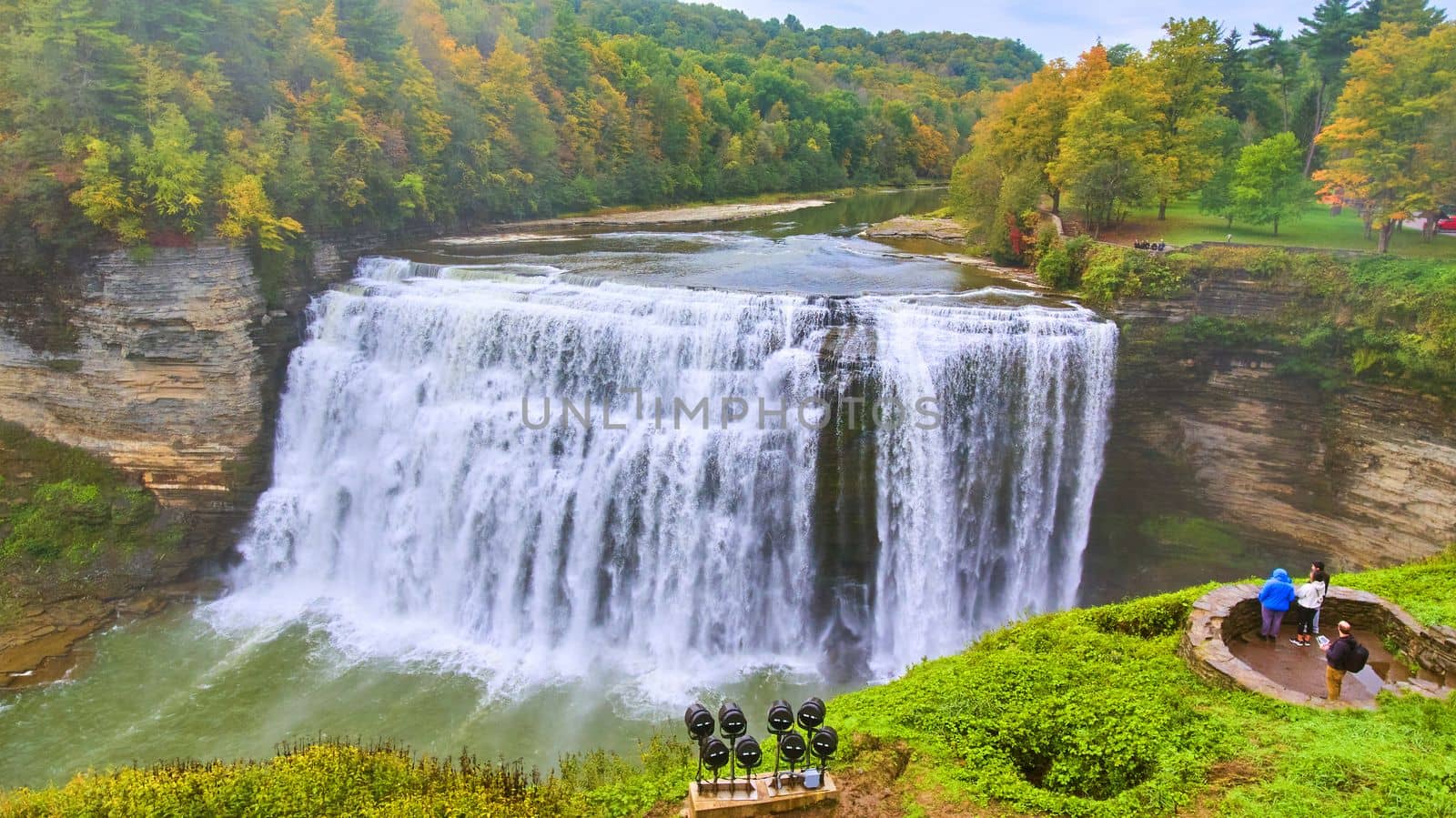 Image of Huge raging waterfall in river through canyon with colorful foliage and tourists admiring from vista
