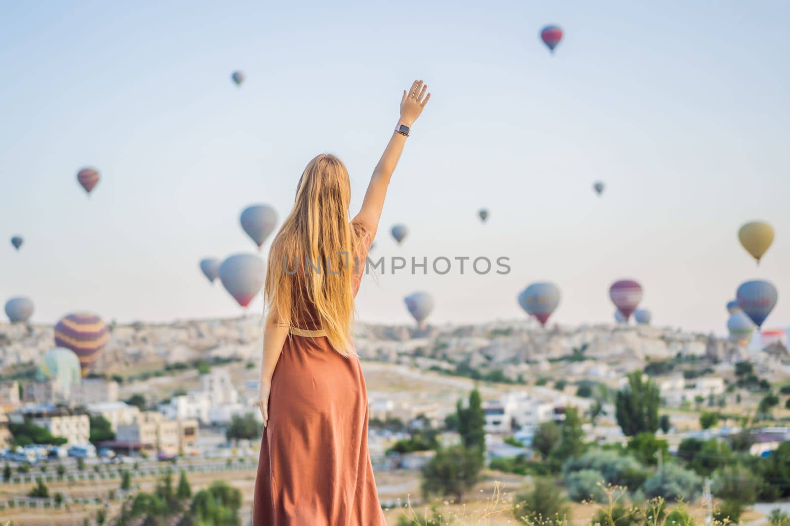 Tourist woman looking at hot air balloons in Cappadocia, Turkey. Happy Travel in Turkey concept. Woman on a mountain top enjoying wonderful view.