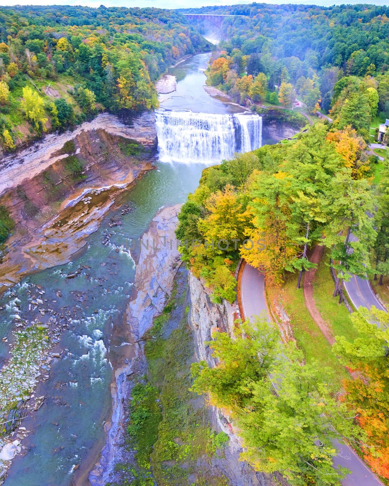 Aerial panorama over road along edge of cliffs with raging waterfall and bridge in background by njproductions