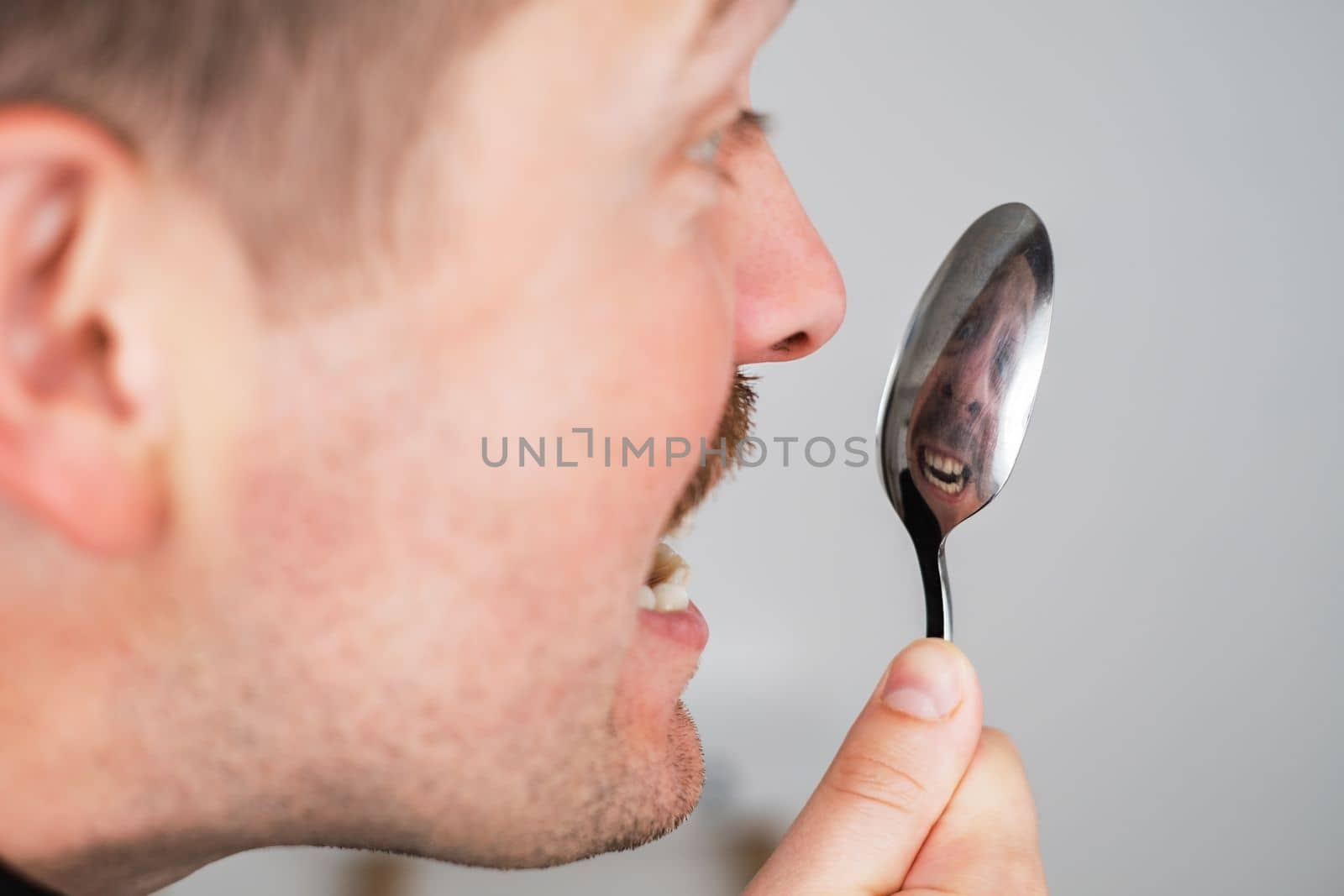 Caucasian man checking his teeth after meal looking on his reflection in spoon.