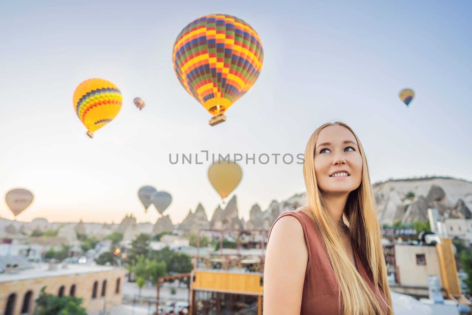 Tourist woman looking at hot air balloons in Cappadocia, Turkey. Happy Travel in Turkey concept. Woman on a mountain top enjoying wonderful view.