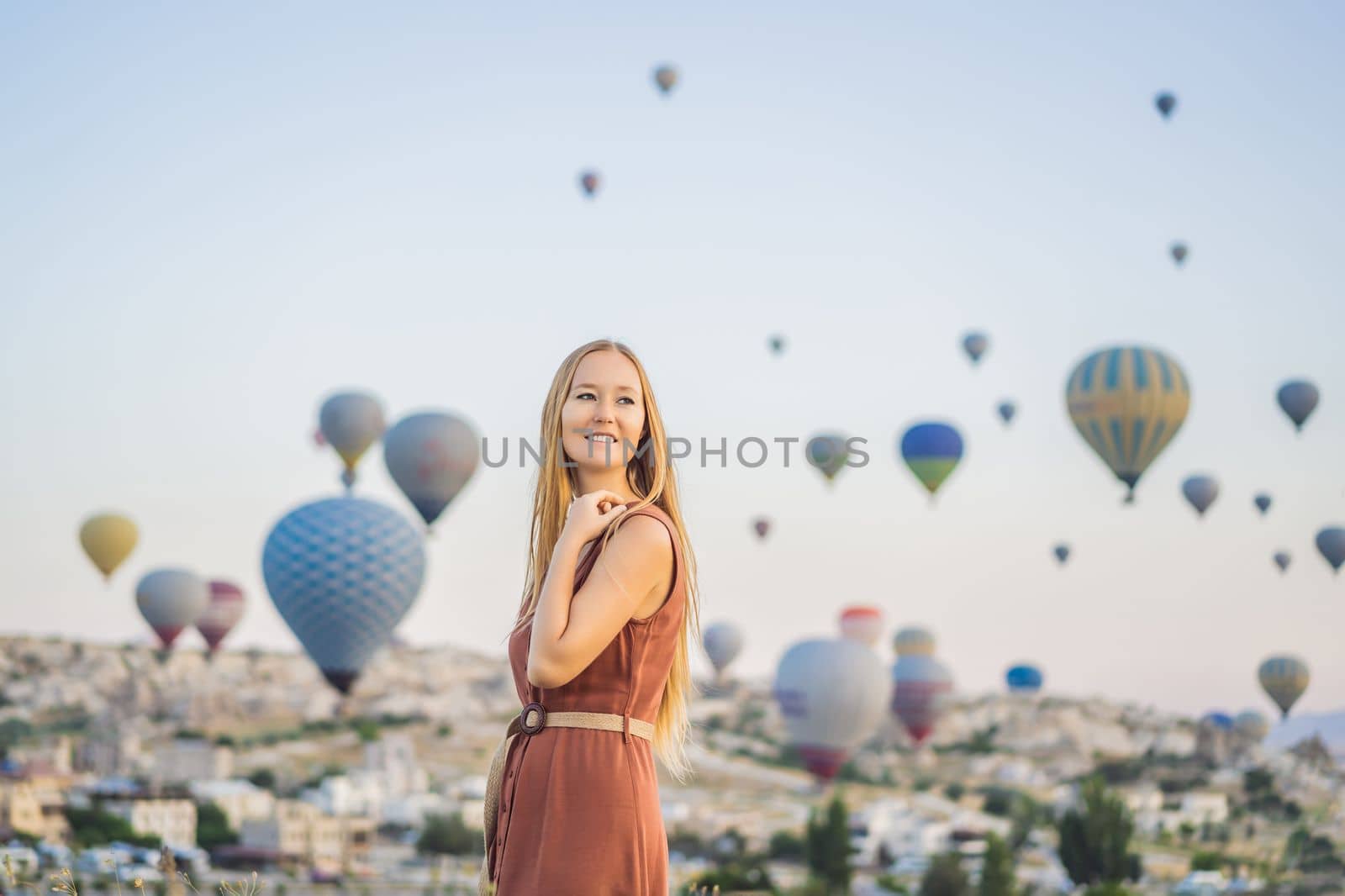 Tourist woman looking at hot air balloons in Cappadocia, Turkey. Happy Travel in Turkey concept. Woman on a mountain top enjoying wonderful view.