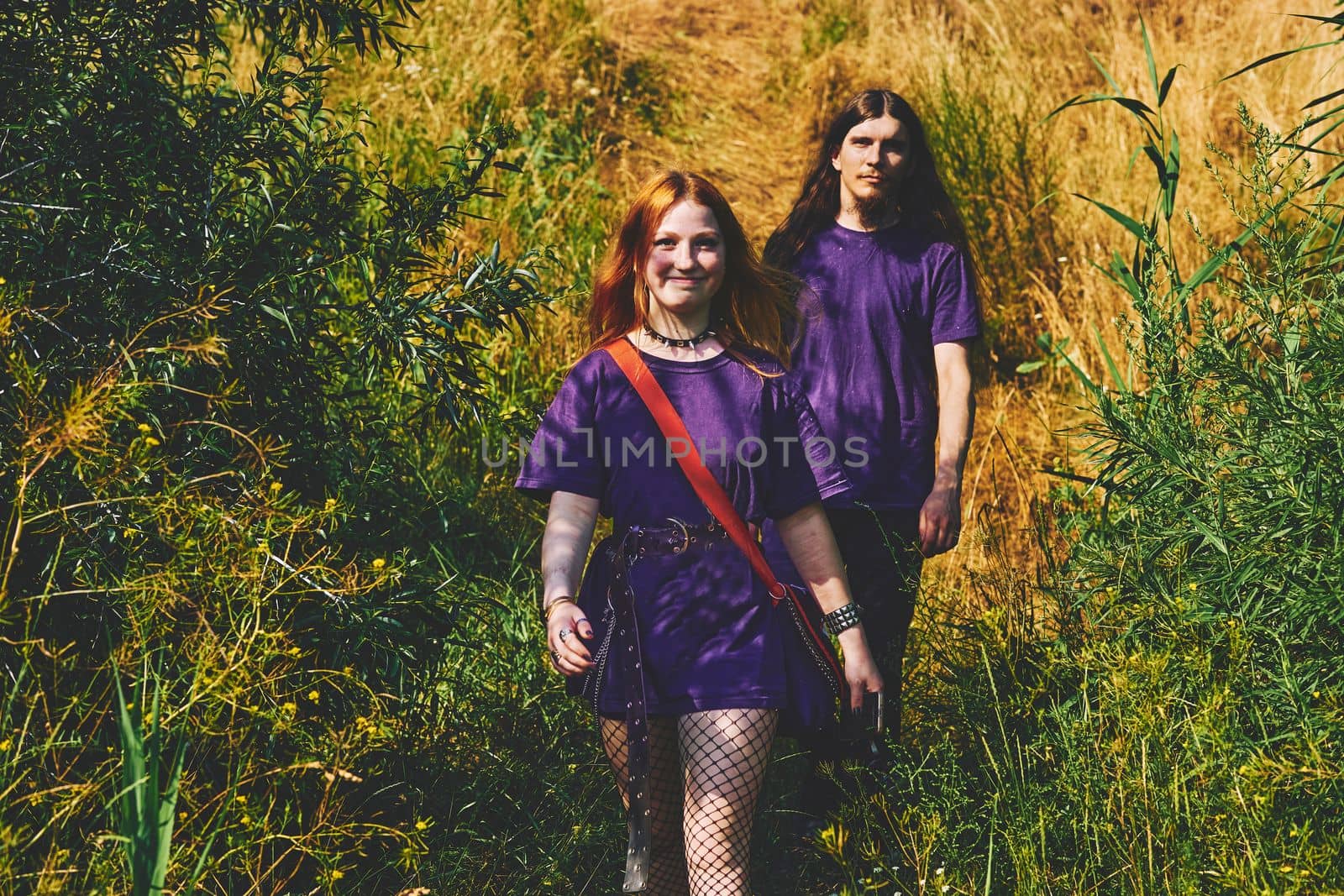 two individuals of the same sort considered together. Young cheerful couple guy and girl in violet purple clothes are walking in the forest.