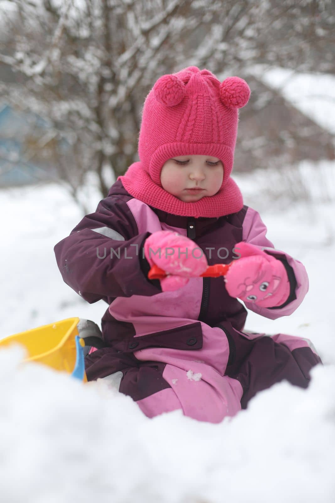 Adorable girl dig snow with shovel and pail on playground covered with snow. little girl playing in the snow.