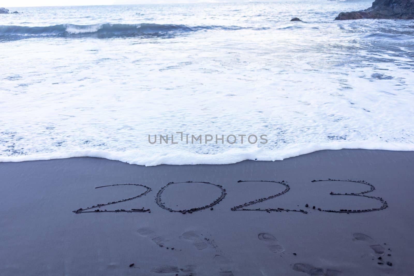 Year 2023 symbol written on black beach sand. High quality photo