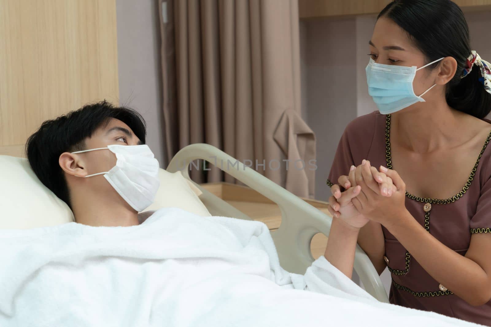 Young patient with attentive visitor and family holding hands in hospital sterile recovery room. The concept of family support for patients receiving hospital care. In-ward medical care and healthcare