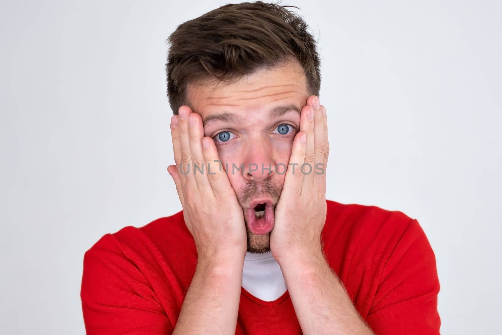 Caucasian man being afraid and shocked, surprise and amazed expression with hands on face. 