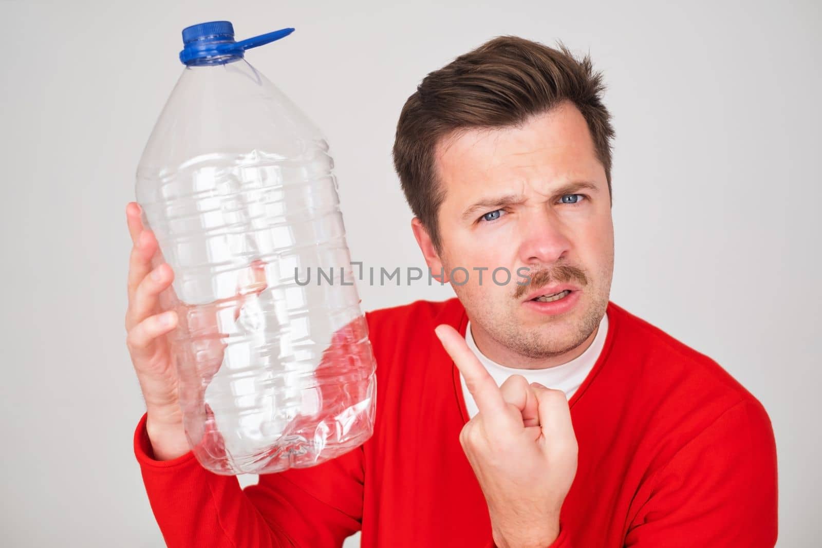Caucasian young man holding empty plastic bottle. Problem with frinking pure water. 