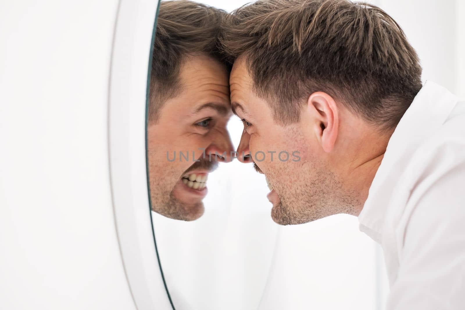 Caucasian man being angry on himself screaming on his reflection on the mirror. Self harm and abuse concept. 
