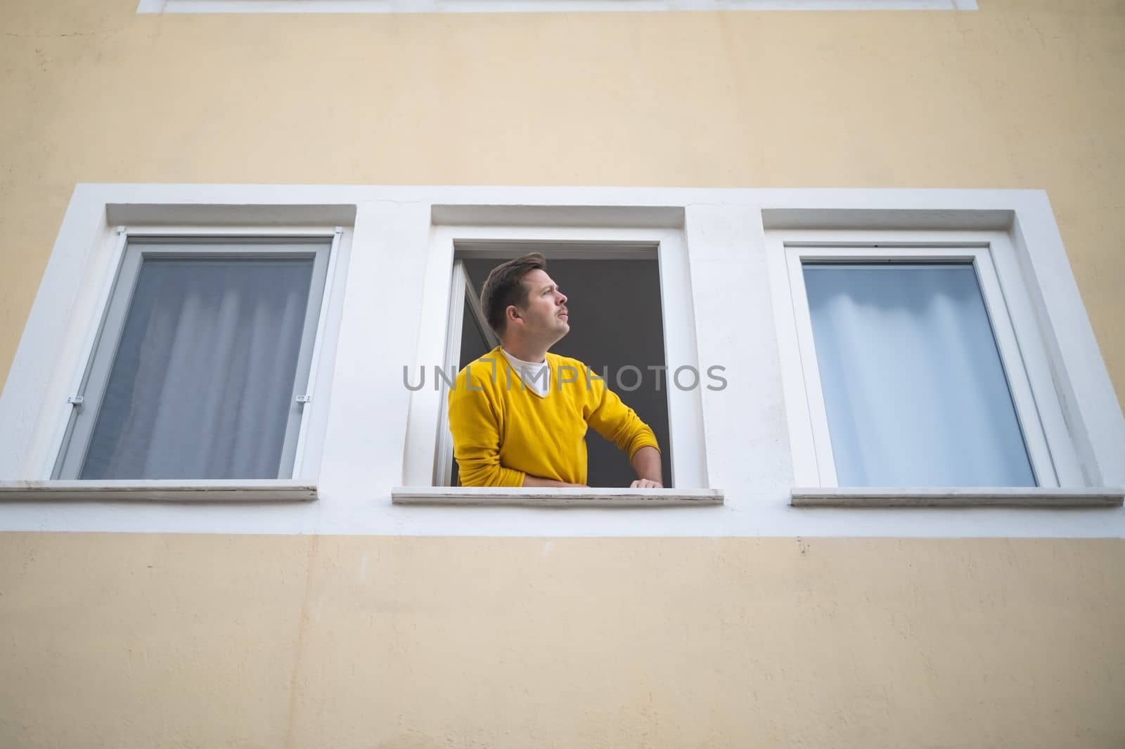 Mature caucasian guy looking from the widnow spying on his neighbours