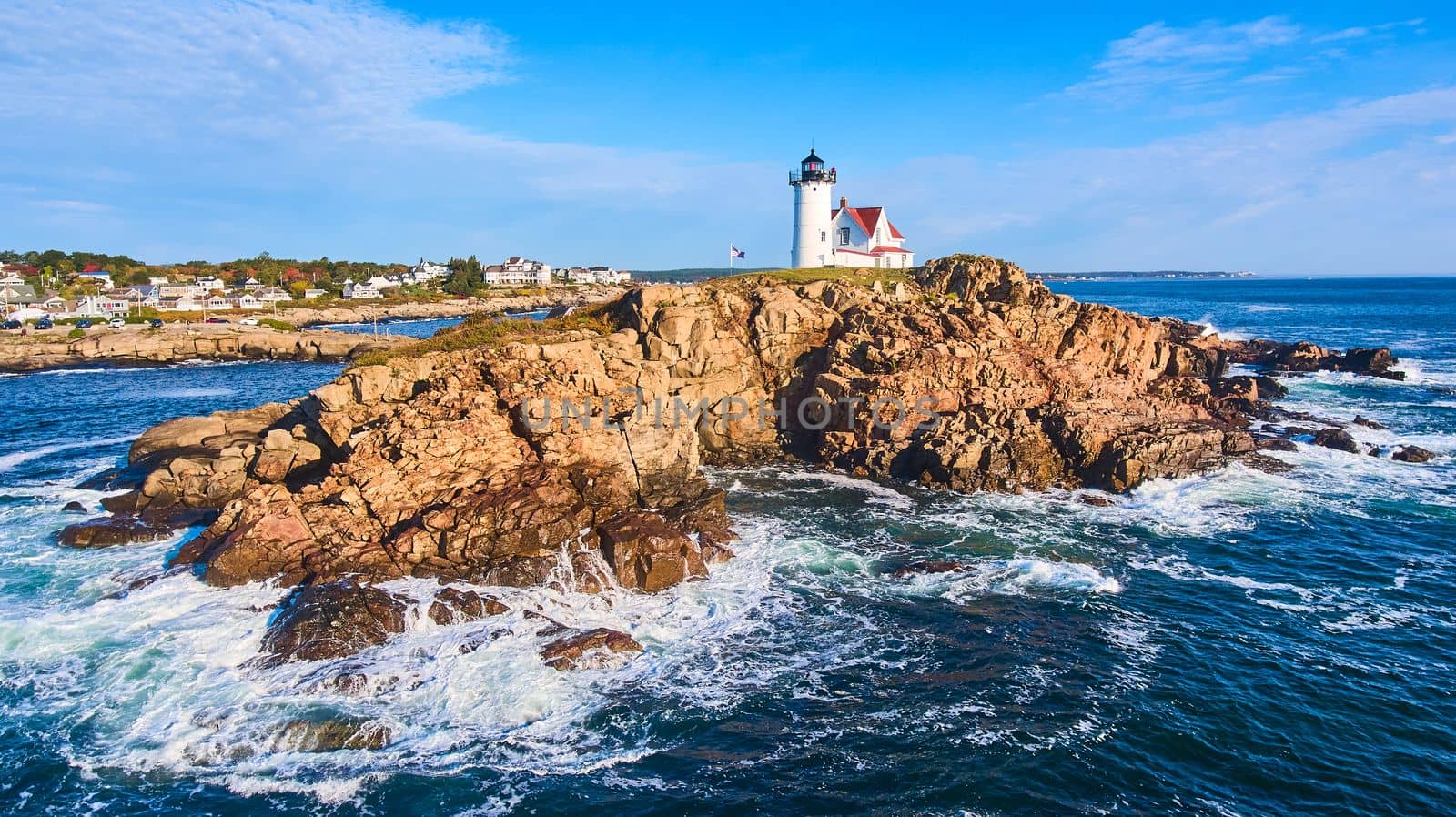 Image of Huge rocky island with lighthouse on Maine coast aerial with waves crashing over rocks