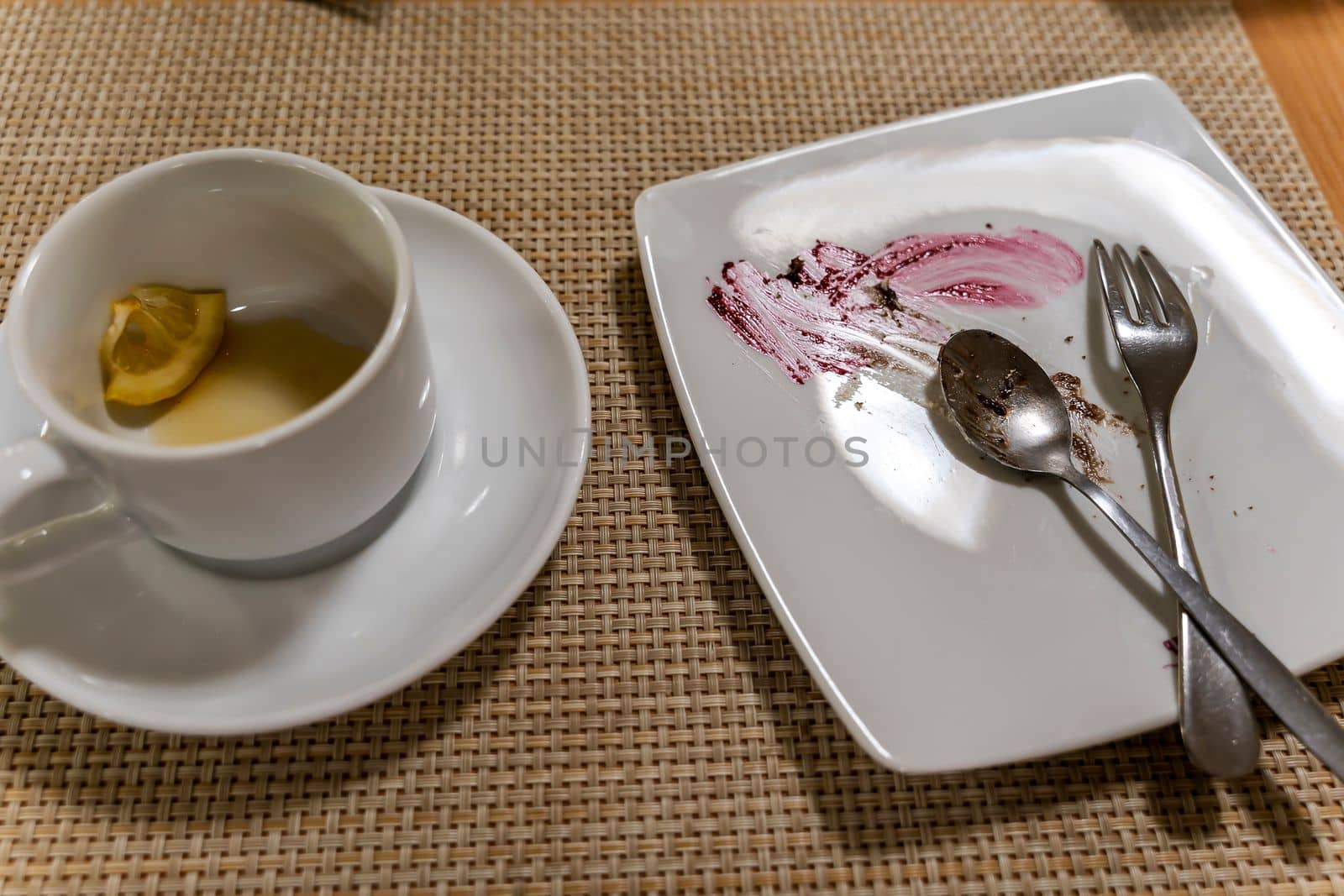 a dirty plate and an empty cup. Empty dishes after eating on a wooden table in a cafe. a white plate with traces of food and a cup with drunk tea and a piece of lemon. after breakfast. morning tea, snack