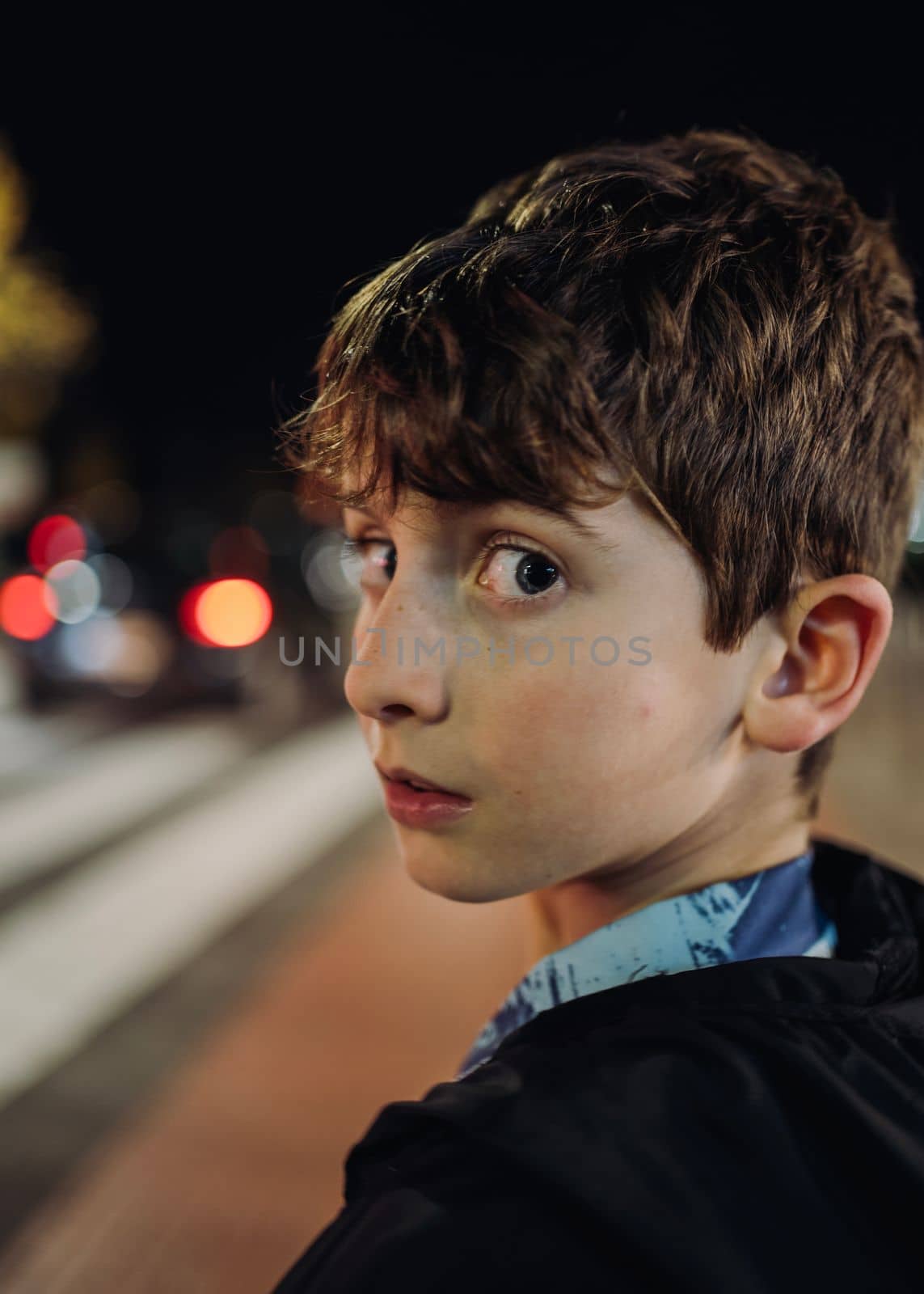 headshot portrait of a young boy lost at night looking back scared.