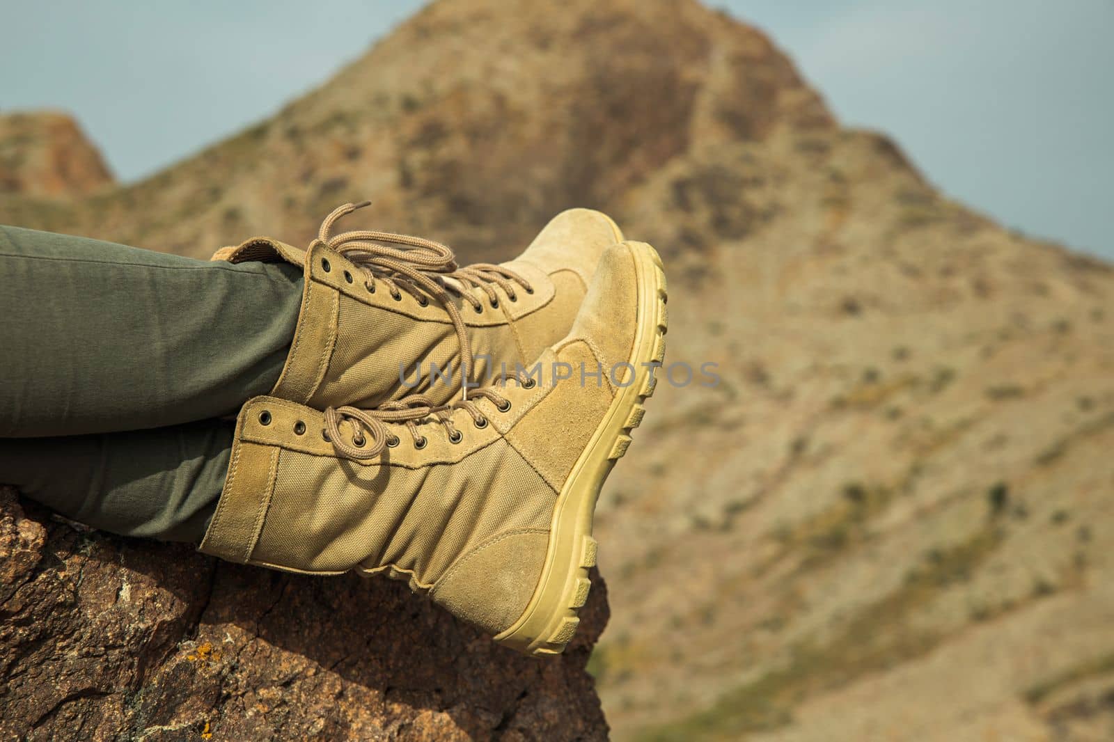 Close-up of traveler female legs with hiking boots relaxing on the rock during trekking.