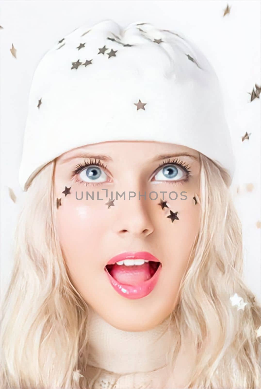 Merry Christmas, happy holidays, a woman playing with confetti stars while wearing a white benny hat, festivity and beauty. Funny blonde girl smiling in a studio portrait as she enjoys the winter holidays, including Christmas and New Year's.