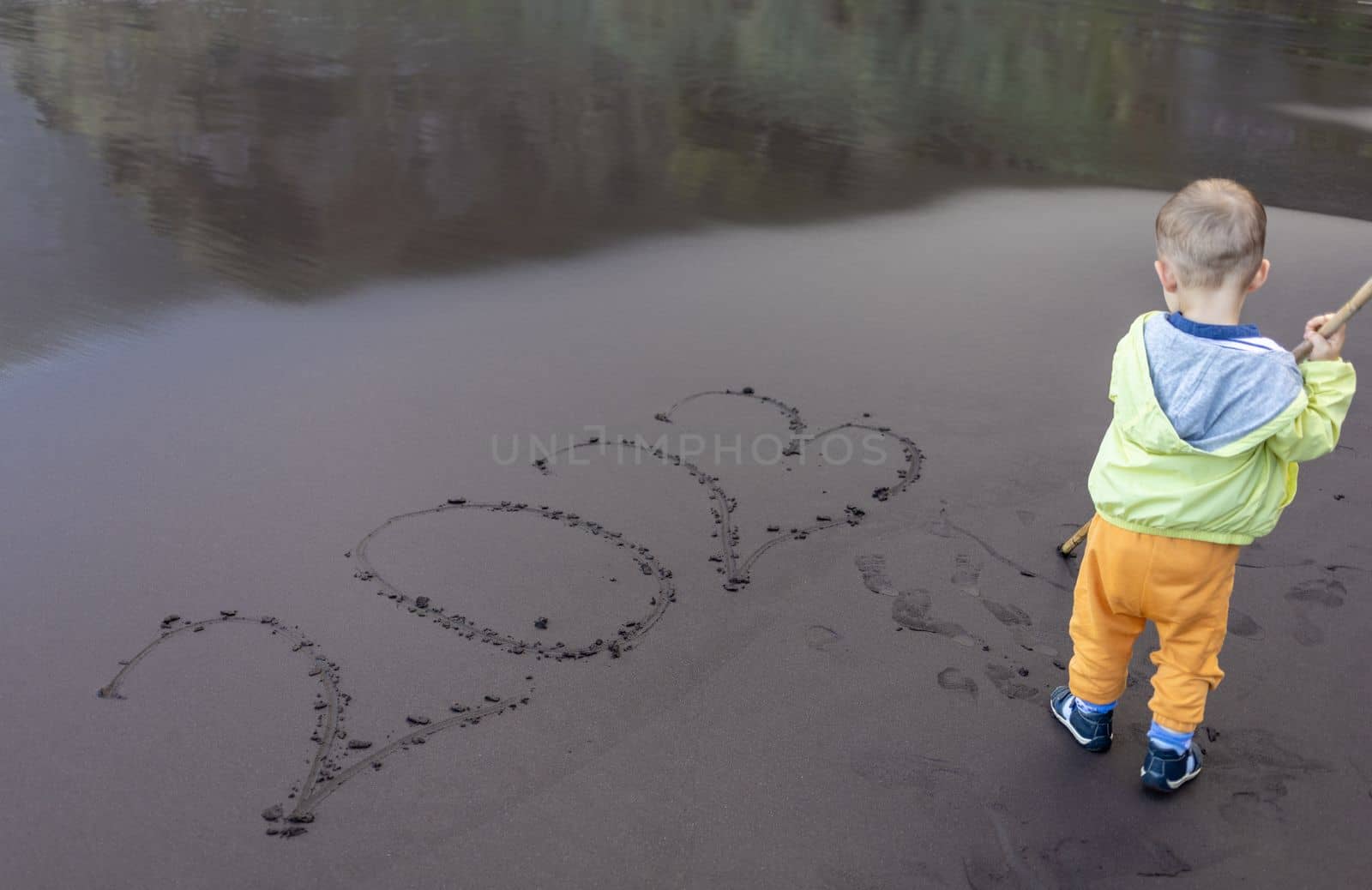 small child writing 2023 year on black beach sand. High quality photo