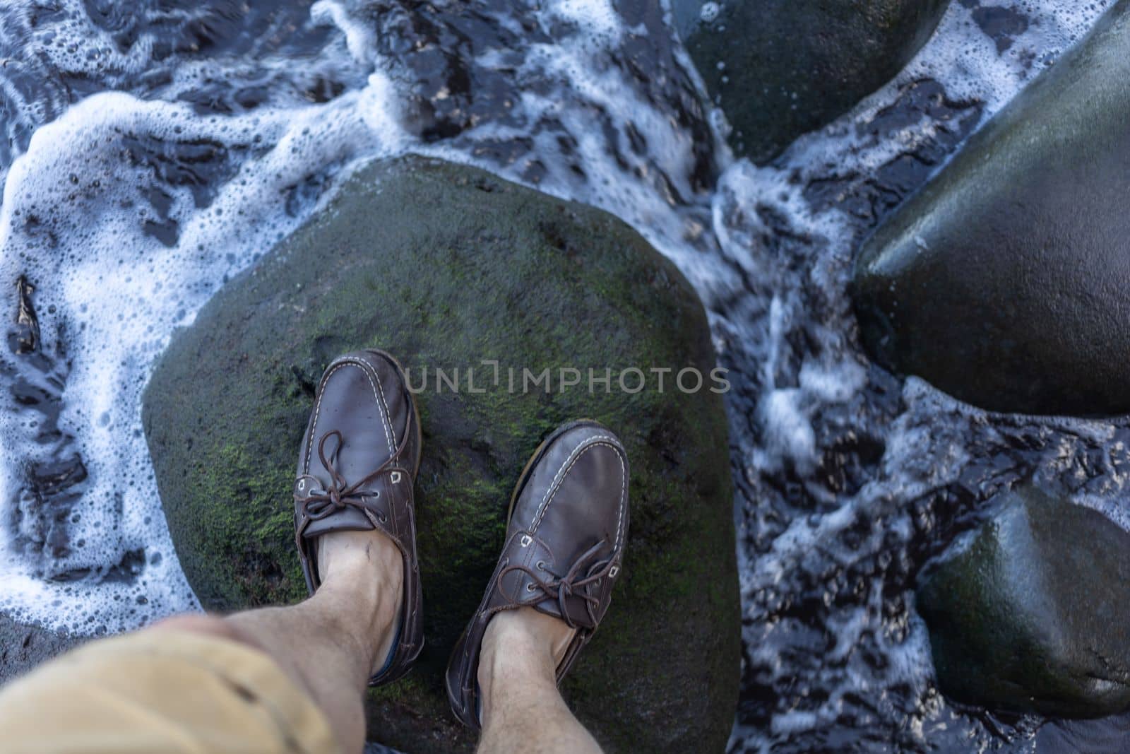 male feet in top siders on green stones over water. High quality photo