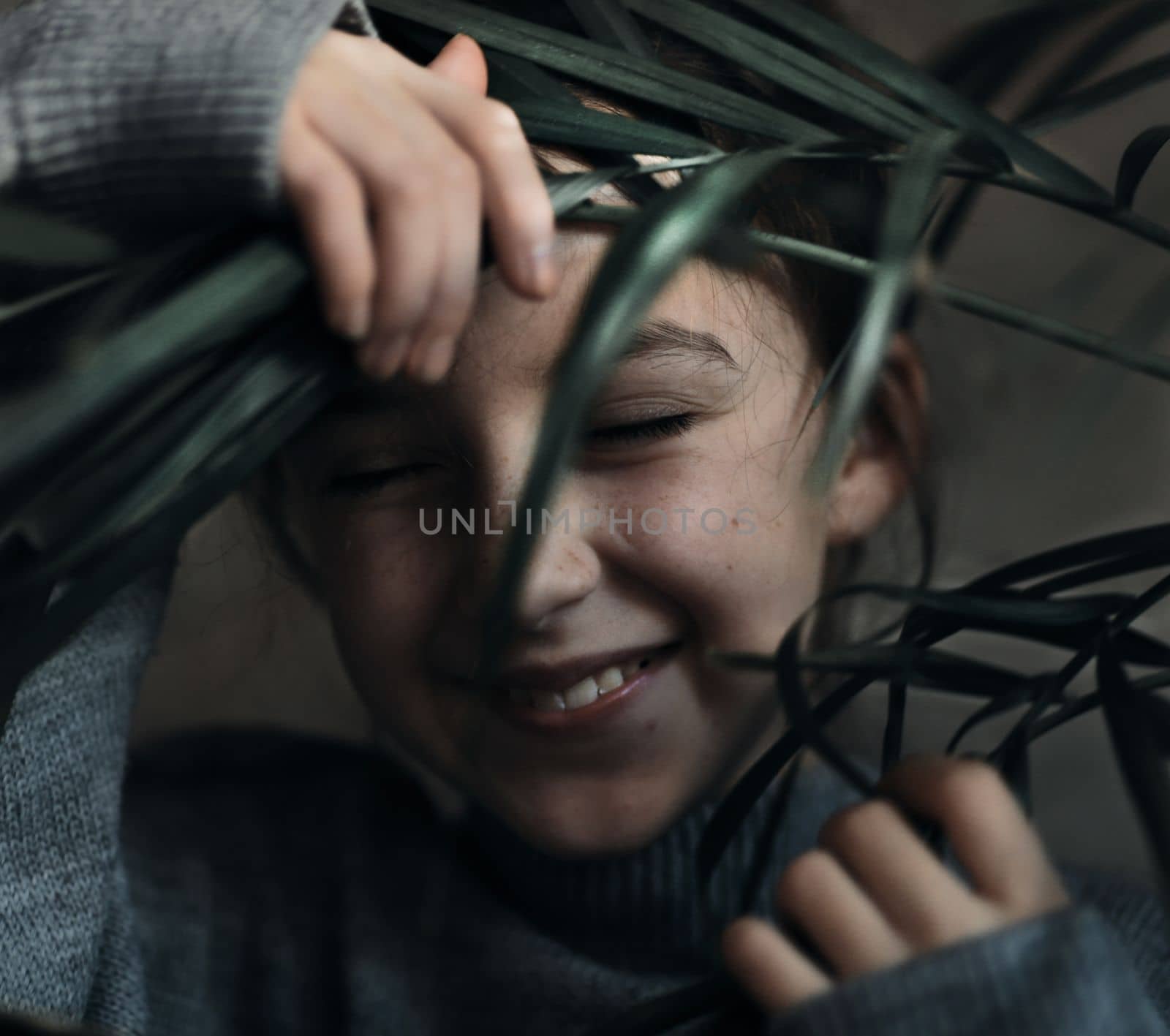 a cheerful child, a charming girl's Face Looking Through The Leaf Of The Plant. High quality photo