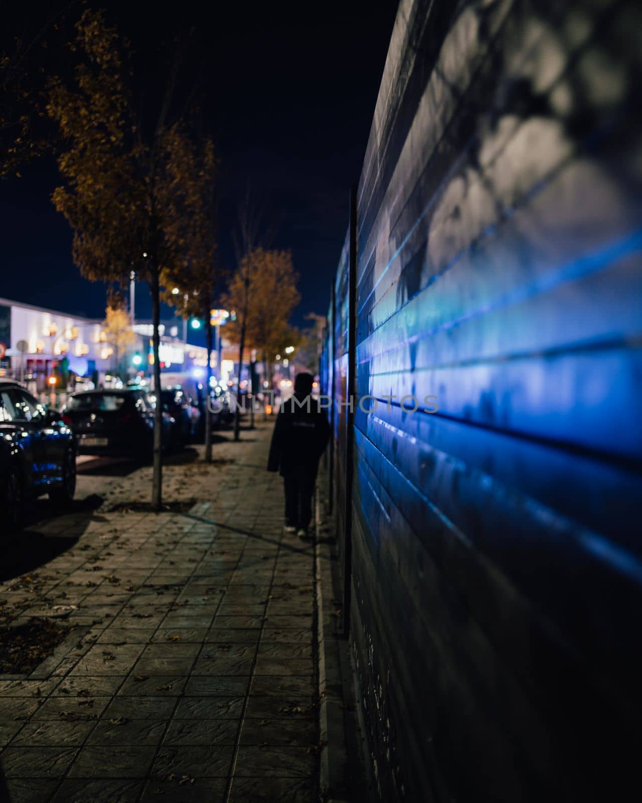 Emergency light reflections at night in wall. Boy walking in darkness towards mall with emergency lights.