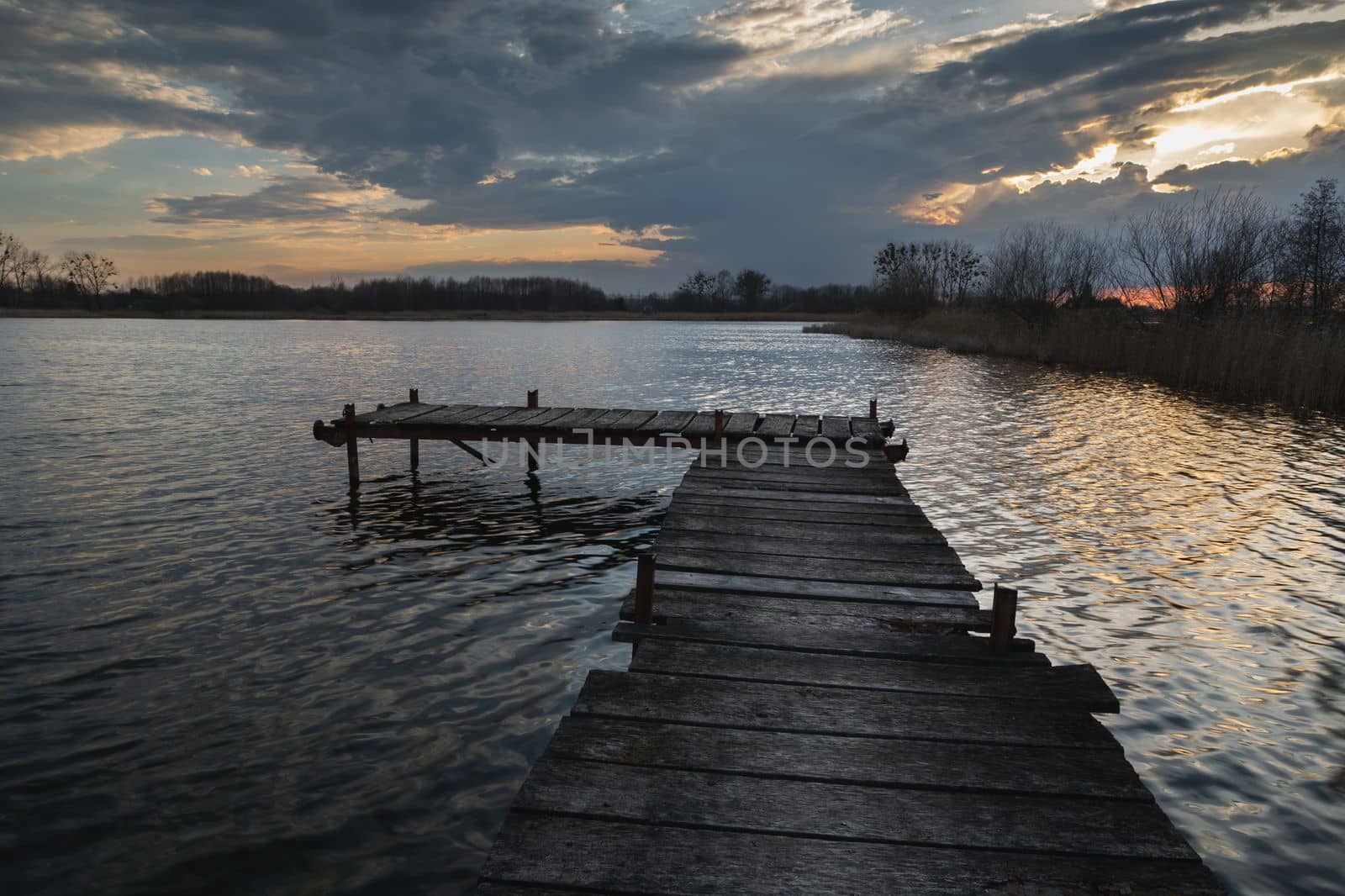 Wooden jetty and lake with evening clouds, water landscape