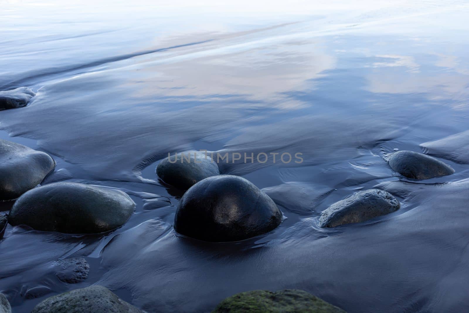 round stones on black wet sand beach with reflection. High quality photo