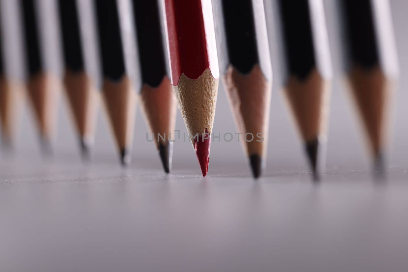 Red pencil stands out from many identical black ones. Uniqueness independence business success concept