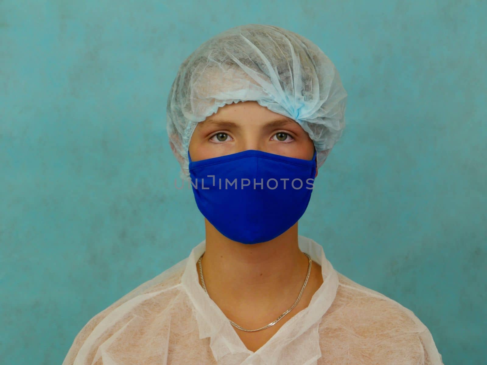 A boy in a white medical gown and a blue protective cap and mask on a blue studio background. Boy The boy uses medical protective equipment against the virus for prevention.