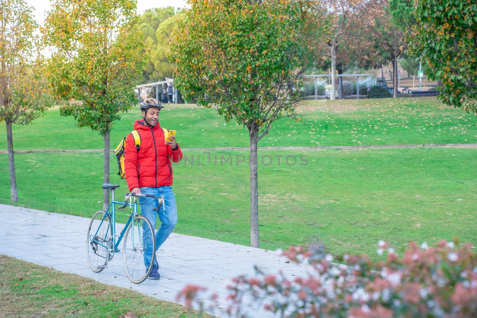 Food delivery concept. Smiling African American driver with backpack looking smartphone in the city by PaulCarr