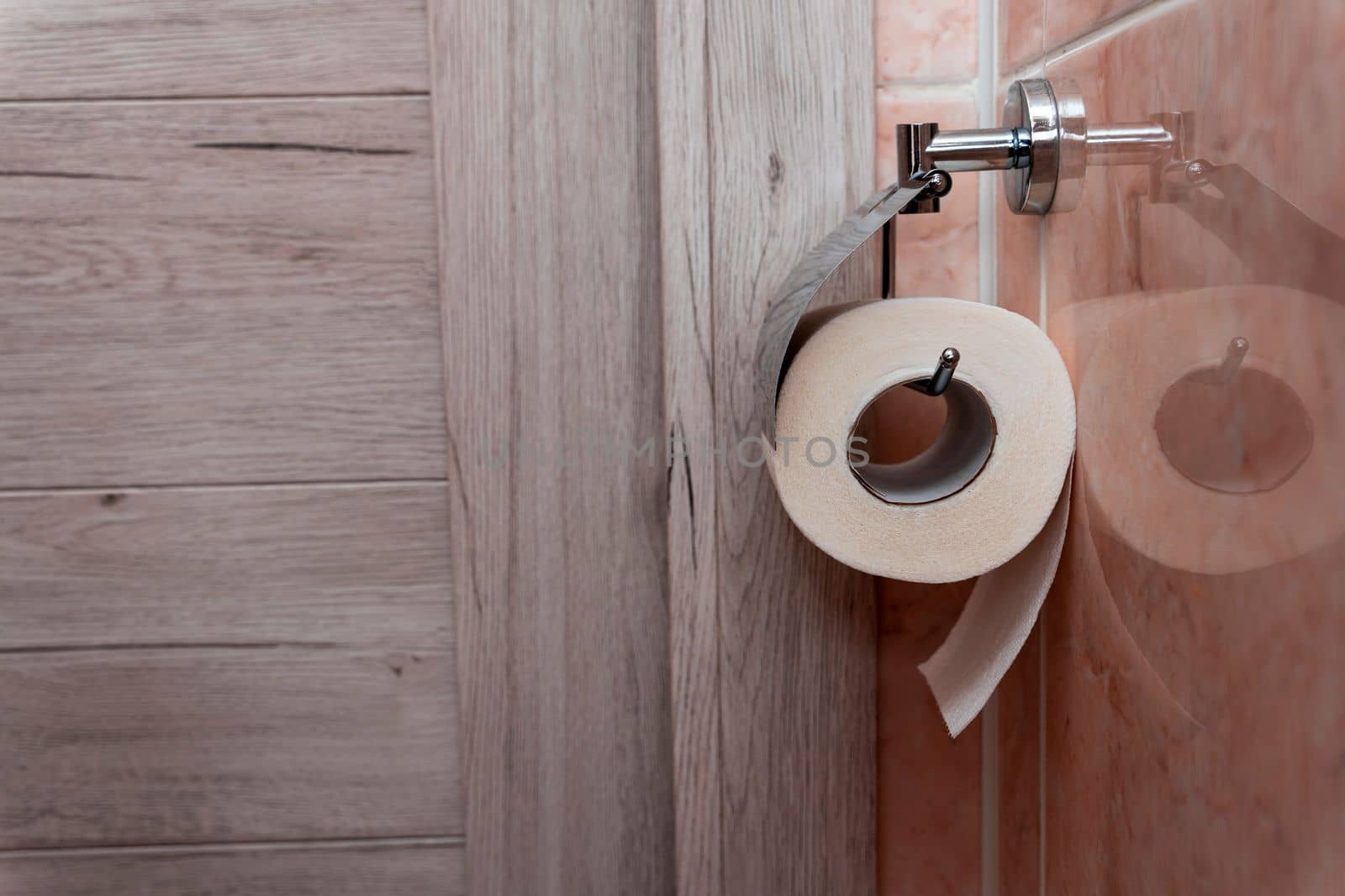 a roll of toilet paper hanging in a holder in the toilet. A roll of soft toilet paper hanging on a modern chrome holder on a toilet wall. High quality photo