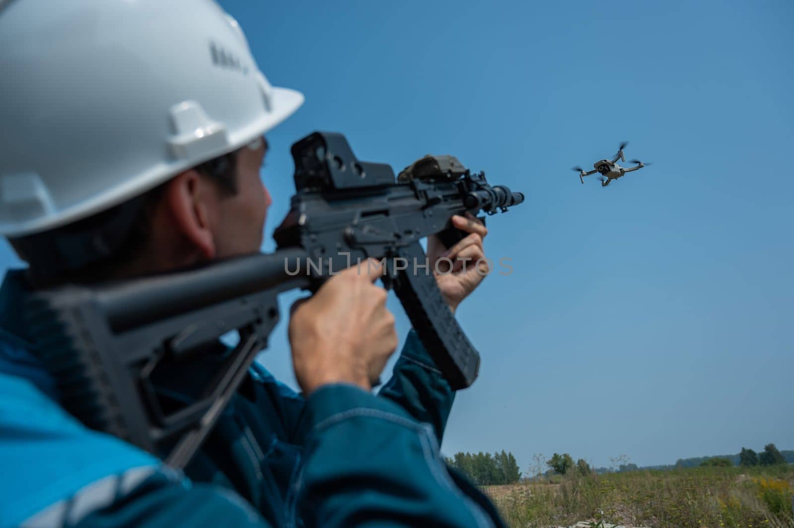 Caucasian man in a helmet shoots a flying drone with a rifle