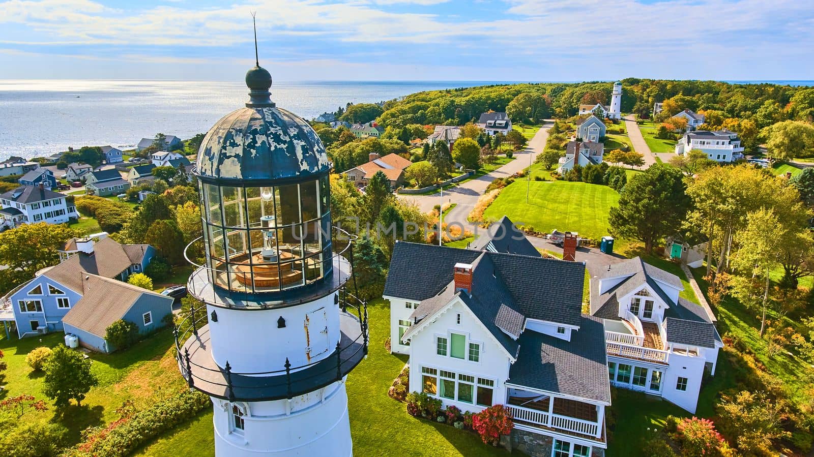 Up close aerial at top of white lighthouse with homes and ocean view in Maine by njproductions